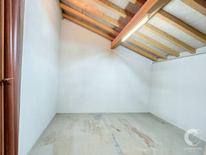 Unfinished attic room with exposed wooden ceiling beams, white walls, and a bare concrete floor; a vertical brown pipe is visible along the left edge.
